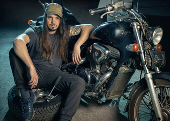 Confident young man in a repair shop sitting in front of a retro motorcycle. Auto mechanic, portrait.