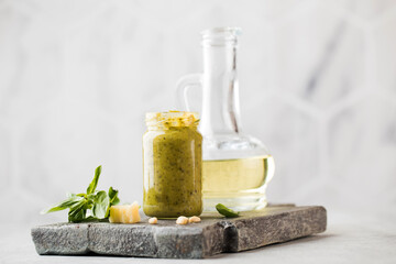 Pesto sauce with green basil leaves, slices of parmesan cheese and a jug of olive oil on a wooden board. Copy space.