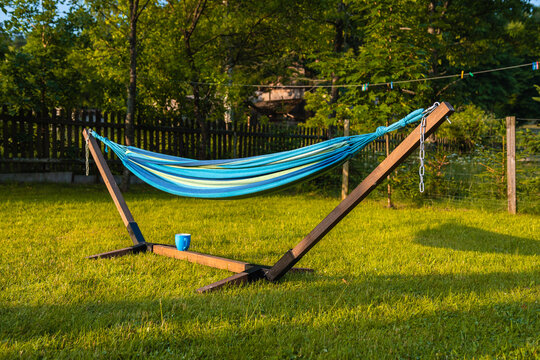 Blue, wooden hammock and blue cup standing on green grass in a rural scenery in the evening sun
