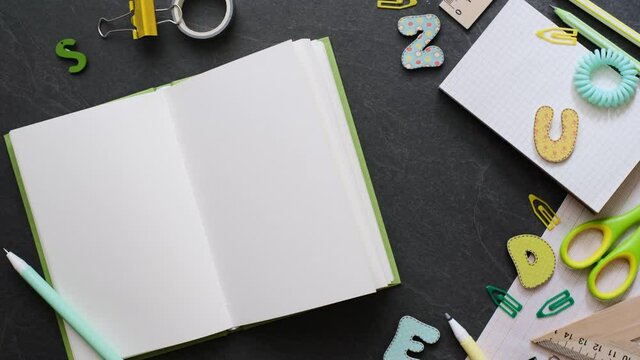 Back to school concept. Person opens empty notebook with school supplies on the black background. Top view with copy space. Working table for creative job, study or planning