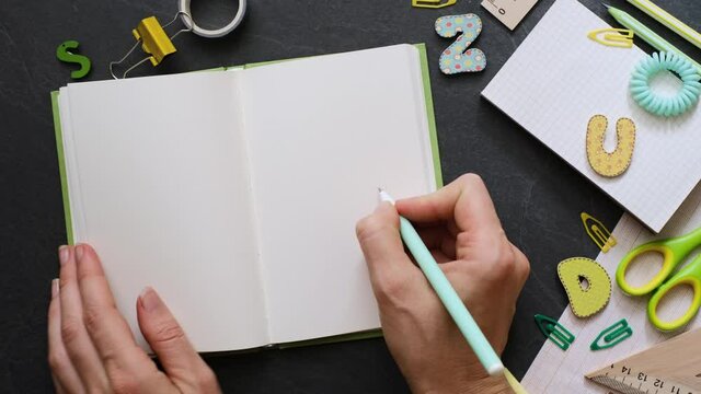 Back to school concept. Person open blank notebook with school supplies on the black background. Top view with copy space. Working table for creative job, study or planning