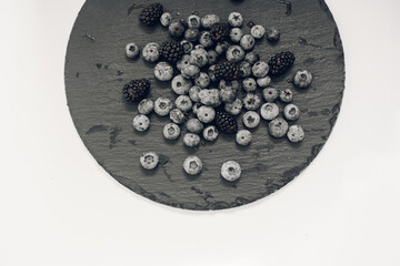 Close-up delicious fresh blueberries lie on a slate plate against black background. Berry picking in the summer season