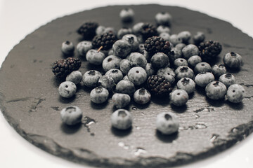 Close-up delicious fresh blueberries lie on a slate plate against black background. Berry picking in the summer season