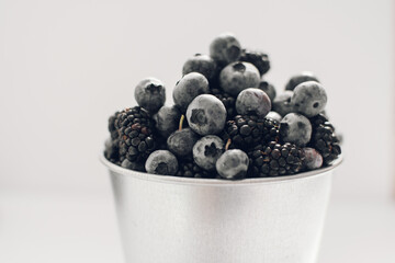 Close-up of delicious fresh blackberries, blueberries in a metal bucket on a white background. Berry picking in the summer season