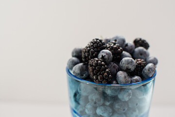 Close-up delicious fresh berries blackberries, blueberries in a glass blue glass on a white background. Collection of berries in the summer season