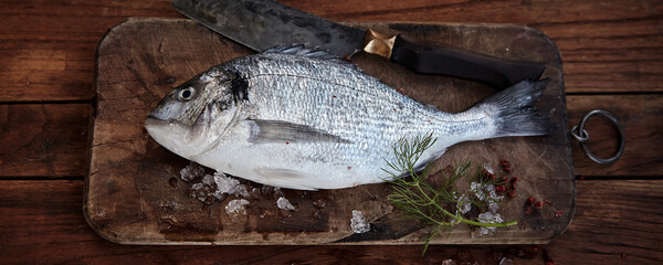 Whole raw fresh bream on a chopping board with cleaver