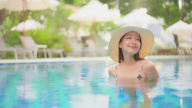 Dreamy scene with beautiful happy asian woman in swimming pool with floppy hat, full frame slow motion