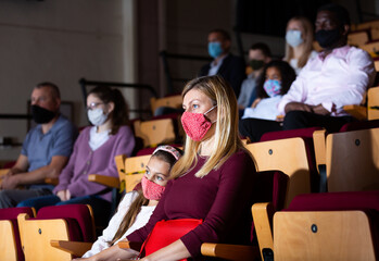 caucasian woman and girl sitting at premiere in theatrical hall during pandemic