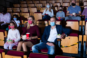parents and children in masks sitting at movie in cinema