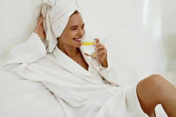 Smiling girl in bathrobe drink lemonade from glass