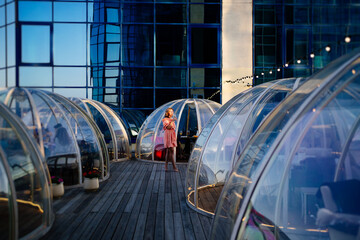 at sunset. woman in a pink dress strolls along the roof between the igloo tables - obrazy, fototapety, plakaty