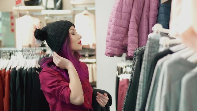 Concept of fashion trends and shopping. Portrait of young woman trying on an outfit in a fashion store fitting room. Beautiful asian girl choosing a black hat looking in the mirror and smiling.