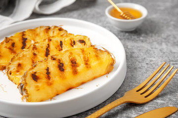 Plate with grilled pineapple slices and honey on grunge background, closeup