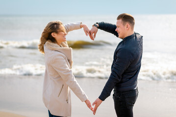 Happy young couple making heart shape with arms on sea beach against spring,autumn evening.