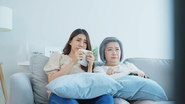 Asian senior mature woman and daughter sitting on sofa watch sad movie