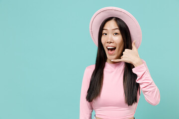 Smiling happy cheery young brunette asian woman 20s wears pink clothes hat doing phone gesture like says call me back isolated on pastel blue color background studio portrait. People emotions concept