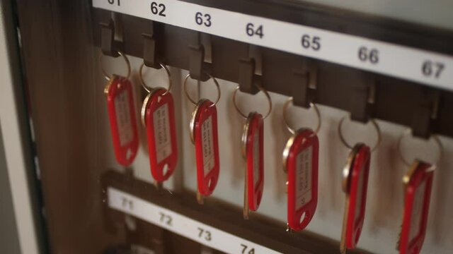 Row of keys with red plastic keychains hang on rack hooks with numbers in brightly lit room extreme close view