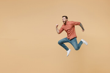Fototapeta na wymiar Full size body length handsome fun tatooed young brunet man 20s short haircut open mouth wears apricot shirt jump like running hurry up look aside isolated on pastel orange background studio portrait