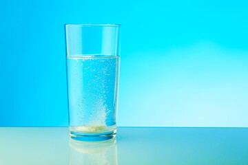 effervescent tablet dissolves in water. a glass of water and fizzy pill on blue background. 