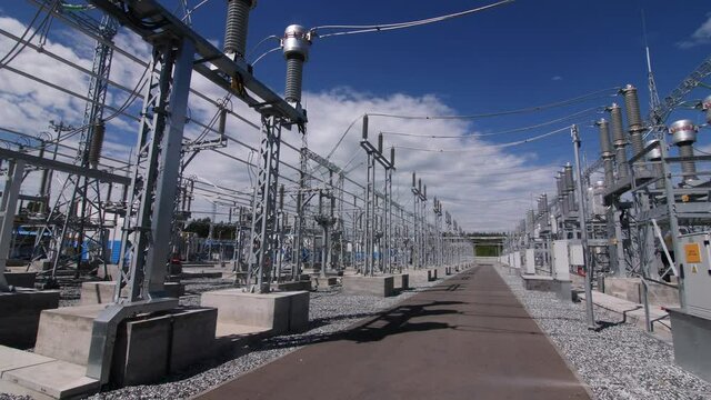 Motion along road across contemporary electricity production substation switchyard under sky with light clouds