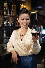 Beautiful smiling woman looking at glass of tasty red wine in her hand