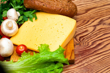 a piece of cheese greens lettuce cherry tomatoes mushrooms and rye buns on a wooden cutting board on the copyspace table