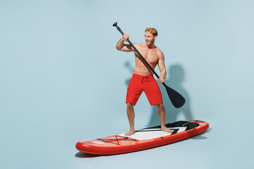 Full length young sexy strong sporty blond man 20s wear red shorts swimsuit standing sup board...