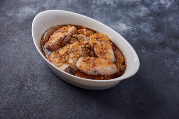 Baked white sea fish in a marinade of olive oil, rosemary, spices in white pan on dark textured background. Close up