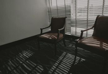 Empty chairs with light and shadow in the room. Furniture for home decoration in vintage style. Empty couple of chair in living room stand on carpet floor near Venetian plastic blinds. Wooden chair.