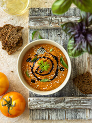 tomato cream soup in a white plate on a wooden board. the concept of summer food, healthy food, fitness food, farm products, seasonal menu, summer menu, vegetarian food