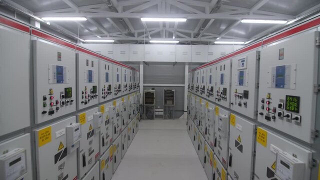Motion between rows of light grey metal cabinets with switchgear in electricity production substation control room