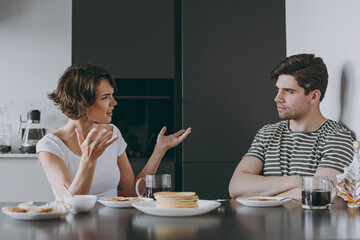 Young indignant sad couple two woman man in casual t-shirt clothes sit table eat pancake with maple...