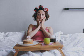 Cheerful fun happy surprised happy young woman wear pajamas hair curlers lying in bed wrap covered...