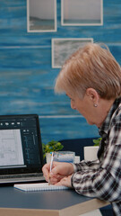 Senior woman architect analysing digital prototype with plans from laptop working from home, taking...