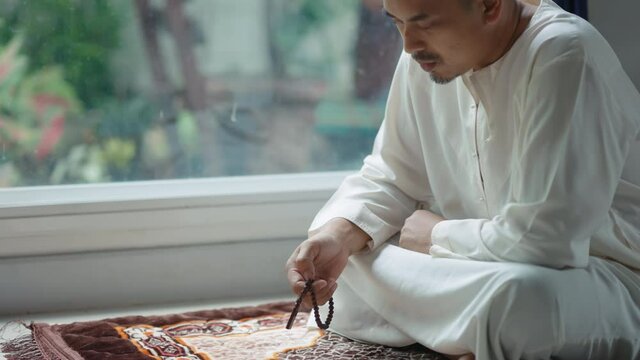 Asian Muslim middle-aged man sitting and reading the Qur'an at his home during the month of Ramadan, 4k resolution.