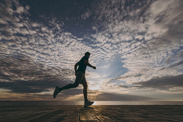 Full body bottom view young sporty athletic fit sportsman man in sports clothes shorts warm up training jog run fast at sunrise sun dawn over sea beach outdoor on pier seaside in summer day morning