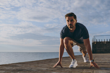 Full body front bottom view young strong sporty toned fit sportsman man 20s in sports clothes shorts warm up training at sunrise sun dawn over sea beach outdoor on pier seaside in summer day morning.