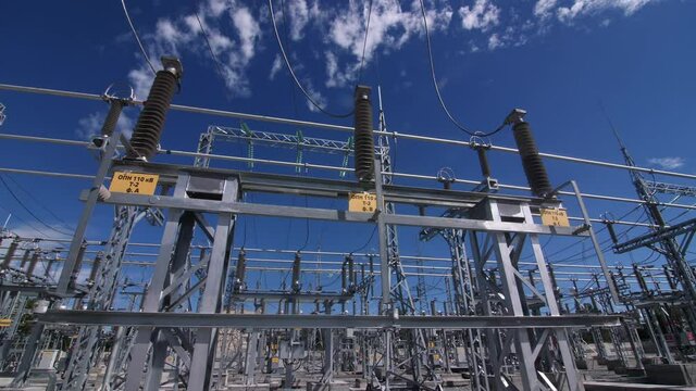 Motion past stand with insulators on electricity production substation switchyard under sky with light clouds closeup