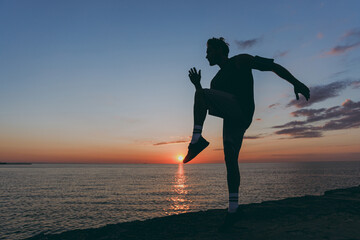 Silhouette side view full body young strong sporty athletic toned fit sportsman man in sports clothes warm up training at sunrise sun dawn over sea beach outdoor on pier seaside in summer day morning.