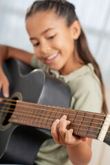 Fototapeta premium Smiling little girl learning to play guitar during lesson at home