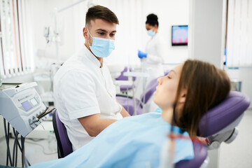 Young dentist communicating with patient before dental exam at dentist's office.