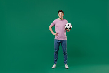 Naklejka na ściany i meble Full size body length young man fan wear basic pink t-shirt cheer up support football sport team hold in hand soccer ball watch tv live stream scream isolated on dark green color background studio
