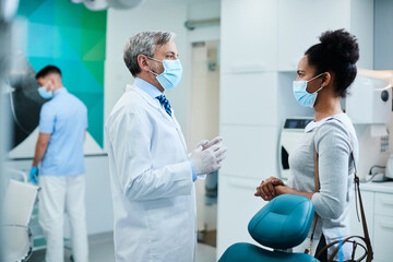 Fototapeta premium African American woman with face mask talking to dentist at dental clinic.