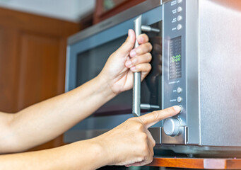 Young woman using microwave oven on shelf.