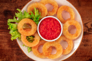 Squid rings close-up on a wooden background. Deep fried calamari rings with green salad and spicy tomato sauce, overhead shot