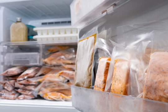 abstract blur and defocused, freezer of modern refrigerator full of frozen food products in quarantine or work from home period during coronavirus pandemic, freeze cooked salmon in vacuum packs
