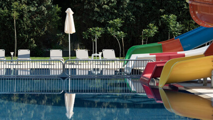 Empty pool area with slide, lounger and umbrella in seaside resort hotel. Exterior of hotel...