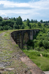 Fototapeta na wymiar Old viaduct in Vorokhta, Carpathians. View from the bridge to the bend and the columns below surrounded by lush greenery