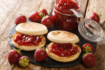 Delicious classic English muffins with strawberry jam close-up on a slate board on the table....
