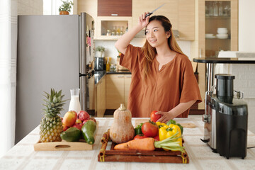 Positive pretty young woman wiping off sweat from her forehead tired of cutting vegetables for dish
